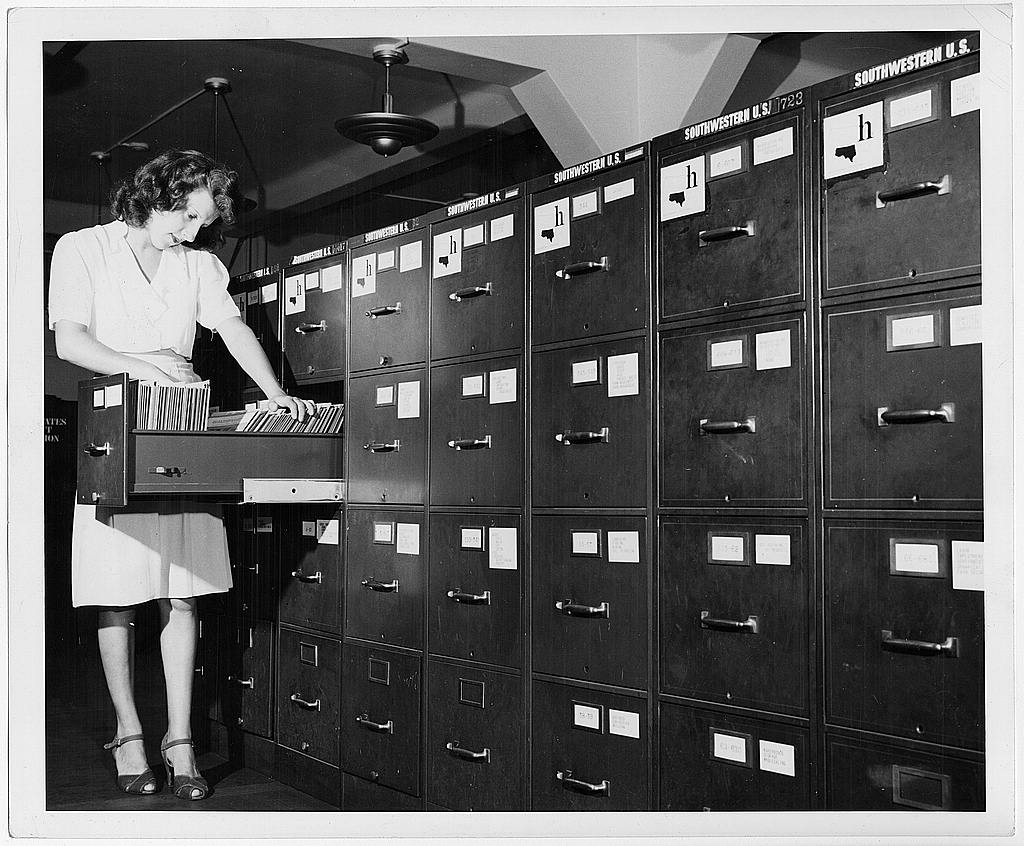 A woman searches through photograph files in a cabinet drawer at the Office of War Information