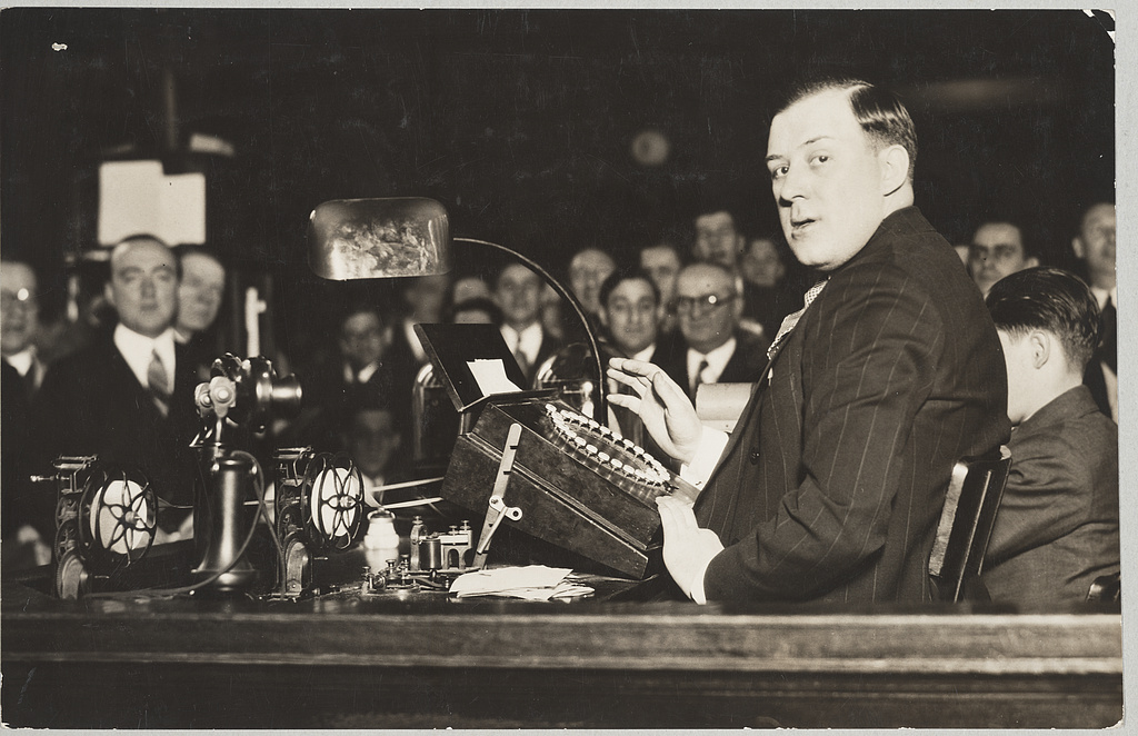 An operator works the master stock ticker as a crowd of men looks on