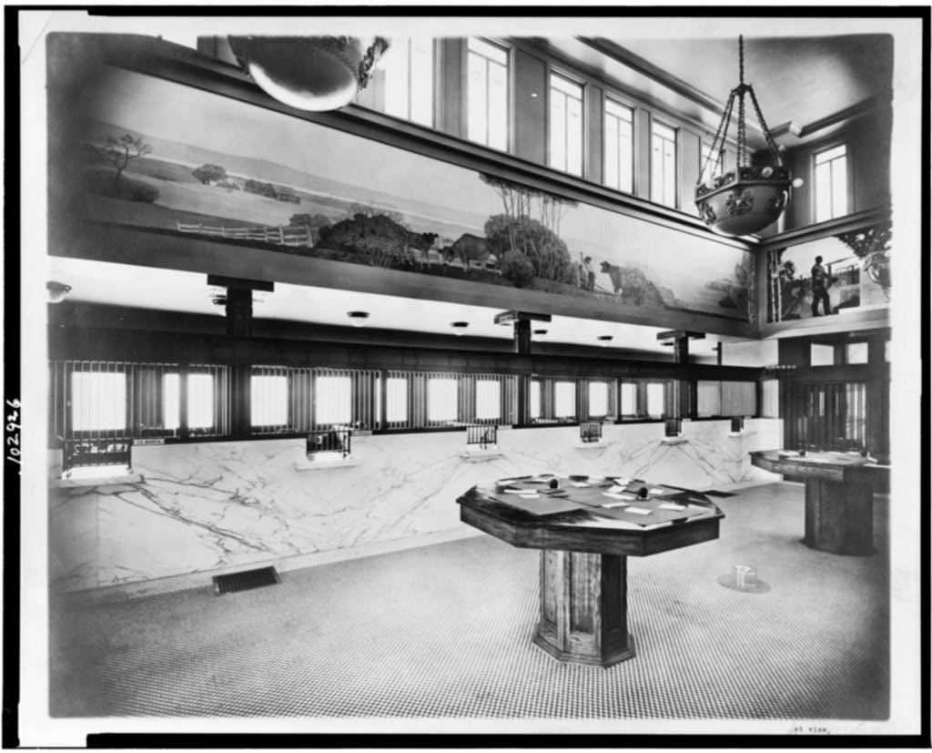 The marble interior of a bank, teller windows beneath a painted mural